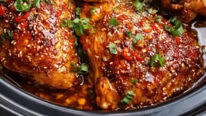 A close-up of sticky honey garlic chili chicken thighs garnished with sesame seeds and scallions.