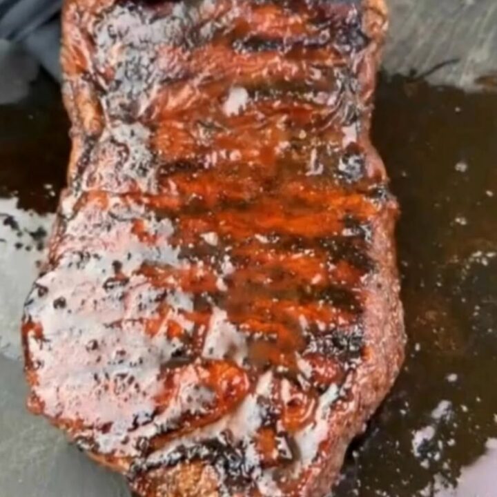 A perfectly grilled steak with visible char marks and a glossy glaze on a wooden cutting board.