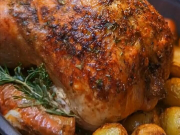 A golden, herb-crusted roast chicken displayed in a dark pan with browned baby potatoes.