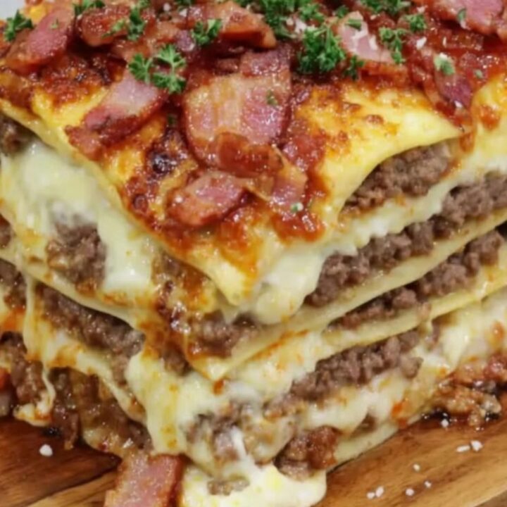 A tall slice of creamy Parmesan garlic bacon lasagna on a wooden board showing distinct layers of meat and cheese