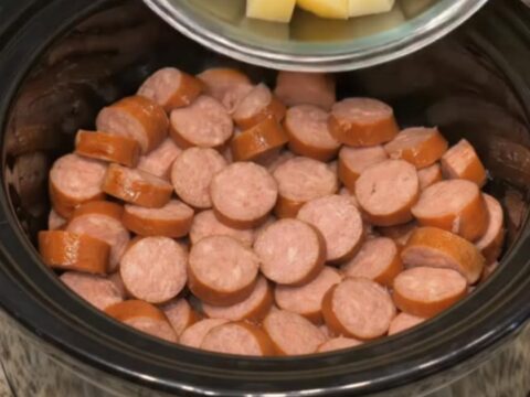 A steaming black slow cooker filled with golden diced potatoes and sliced smoked sausage.