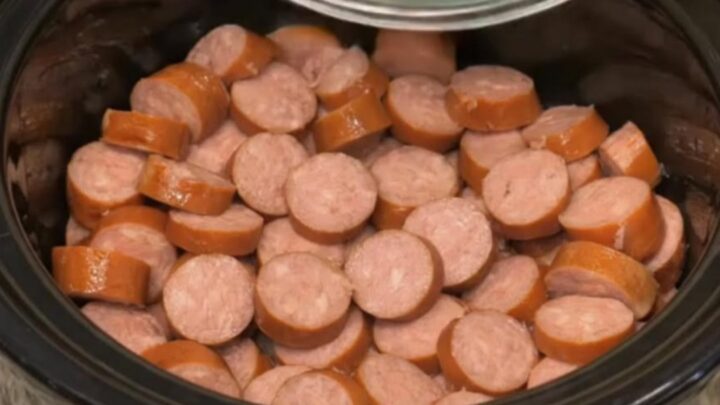 A steaming black slow cooker filled with golden diced potatoes and sliced smoked sausage.
