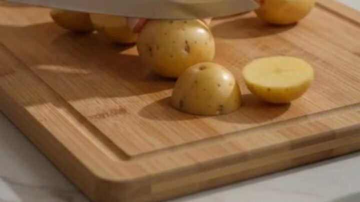 A metal spatula lifting a portion of golden, crispy garlic parmesan roasted baby potatoes from a baking sheet.