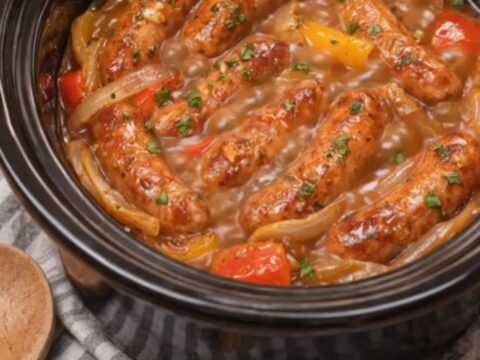 Juicy Italian sausages and colorful bell peppers in a rich tomato sauce inside a black slow cooker.