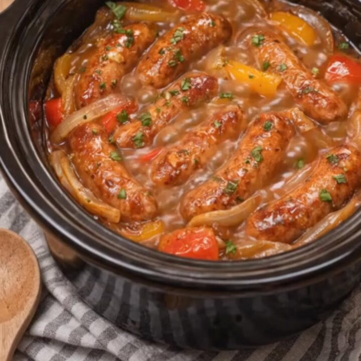 Juicy Italian sausages and colorful bell peppers in a rich tomato sauce inside a black slow cooker.