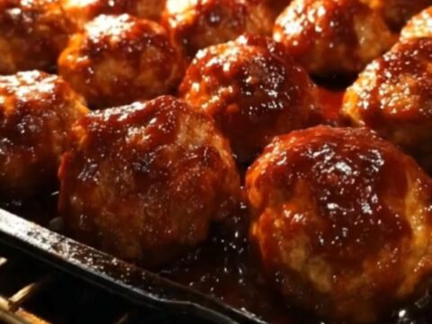 A close-up of glossy, glazed meatballs on a baking tray just out of the oven.