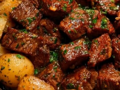 A white plate featuring tender, glossy beef bites and golden potatoes in a savory garlic butter sauce.