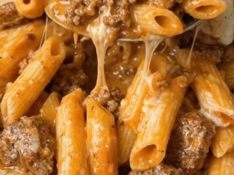 A close-up of a cheesy ground beef penne bake in a baking dish with melted cheddar cheese.
