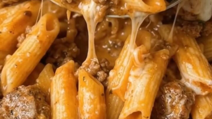 A close-up of a cheesy ground beef penne bake in a baking dish with melted cheddar cheese.