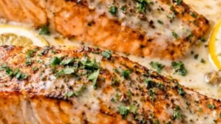 A golden-seared salmon fillet in a creamy lemon garlic sauce on a white plate.