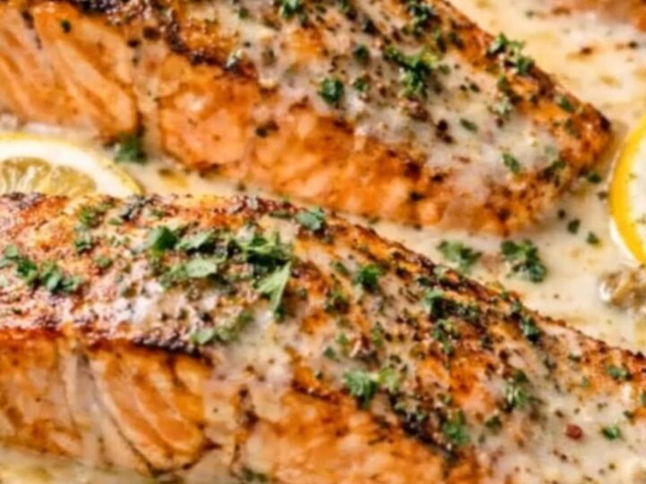 A golden-seared salmon fillet in a creamy lemon garlic sauce on a white plate.