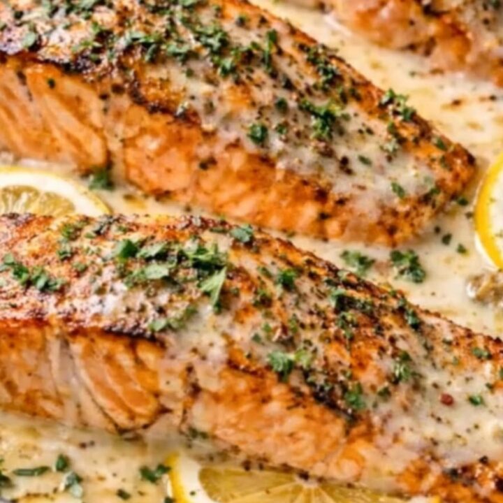 A golden-seared salmon fillet in a creamy lemon garlic sauce on a white plate.