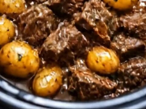 A steaming portion of beef bites and potatoes in a rich gravy served in a white bowl.