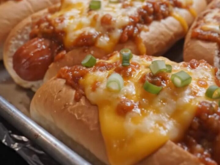 A close-up of a crispy cheesy baked hot dog on a white plate with melted cheese stretching from the bun.
