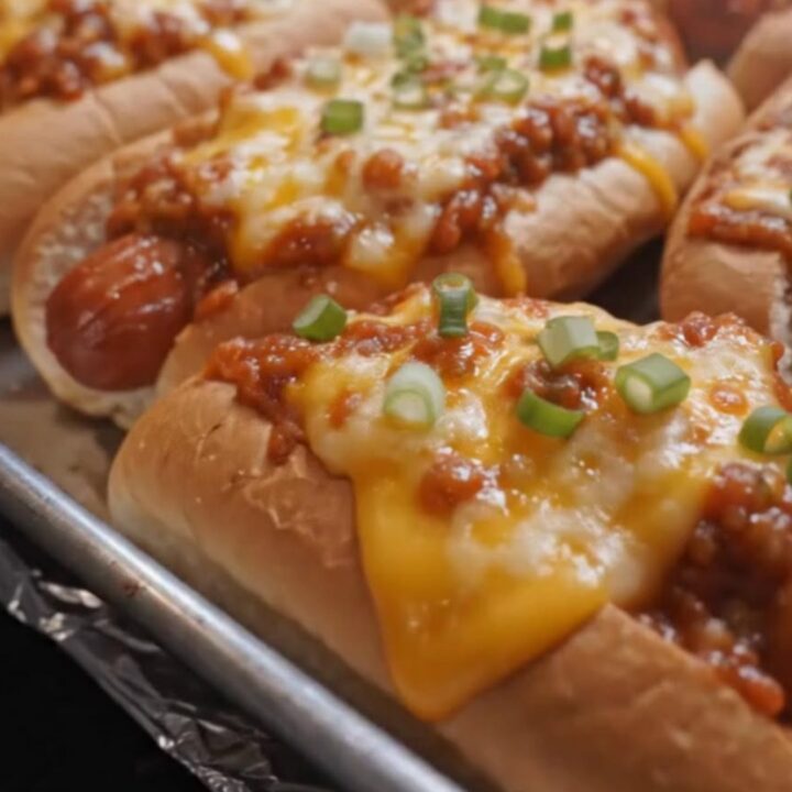 A close-up of a crispy cheesy baked hot dog on a white plate with melted cheese stretching from the bun.