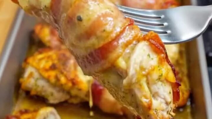 A close-up of golden-brown bacon wrapped garlic parmesan chicken sliced on a cutting board with steam rising