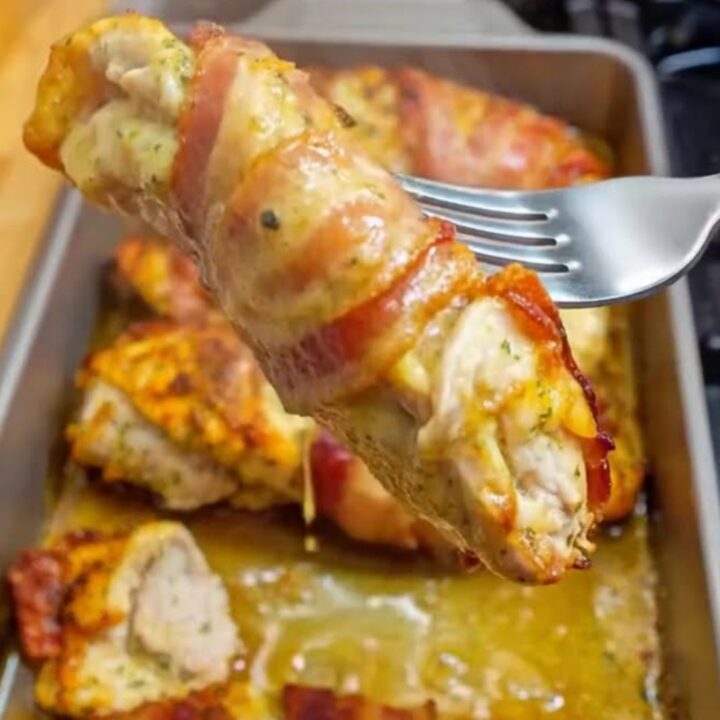 A close-up of golden-brown bacon wrapped garlic parmesan chicken sliced on a cutting board with steam rising