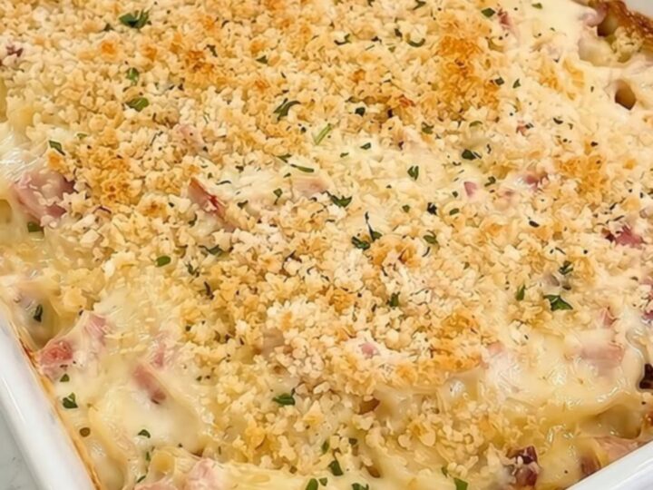 A steaming scoop of creamy chicken cordon bleu pasta casserole in a white ceramic dish.
