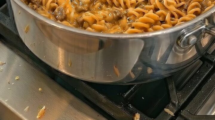 A large stainless steel pot filled with creamy beef and fusilli pasta with melted cheese.