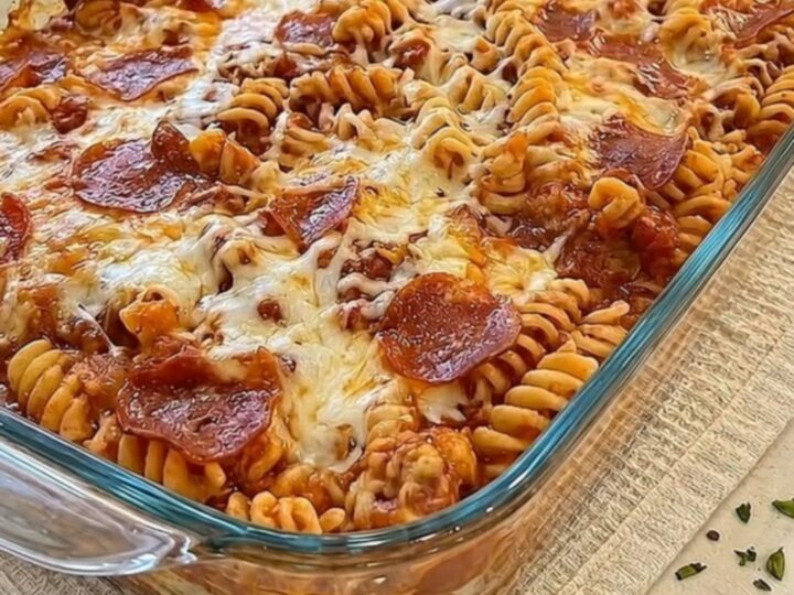 A bubbly and cheesy pizza pasta bake in a glass dish with long strands of melted mozzarella.