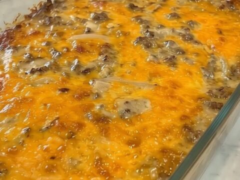 A golden-brown cheesy ground beef and potato casserole served in a glass baking dish.