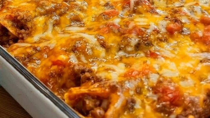 Steaming cheesy beef enchilada casserole scooped from a 9x13 glass baking dish with an impressive cheese pull.