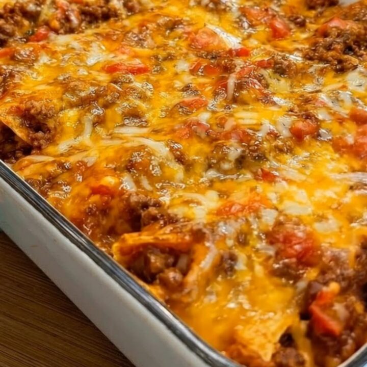 Steaming cheesy beef enchilada casserole scooped from a 9x13 glass baking dish with an impressive cheese pull.
