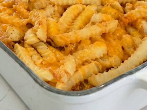 A golden cheeseburger casserole in a white baking dish topped with crispy crinkle-cut fries and melted cheddar.