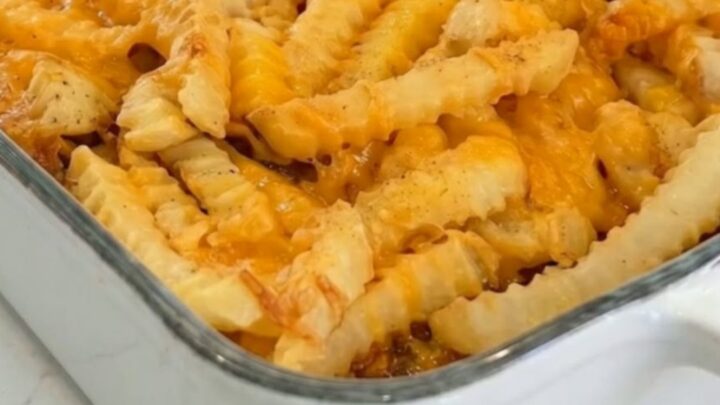 A golden cheeseburger casserole in a white baking dish topped with crispy crinkle-cut fries and melted cheddar.