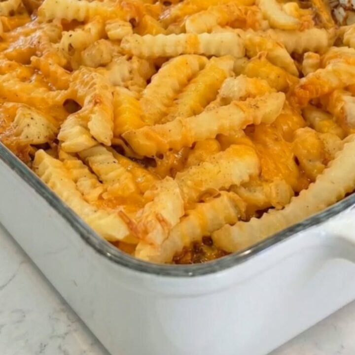 A golden cheeseburger casserole in a white baking dish topped with crispy crinkle-cut fries and melted cheddar.