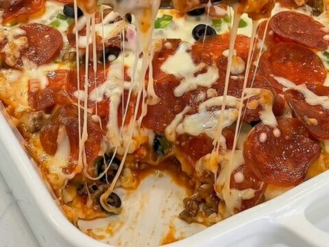 A golden-brown bubble up pizza bake in a white ceramic dish with melted cheese stretching from a serving slice.
