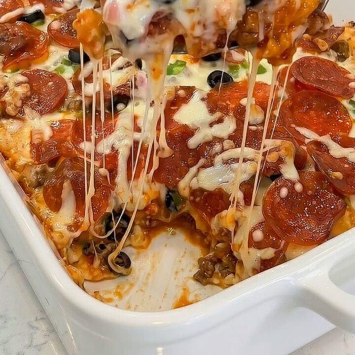 A golden-brown bubble up pizza bake in a white ceramic dish with melted cheese stretching from a serving slice.