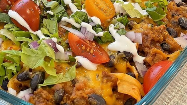 A warm walking taco casserole in a glass dish topped with melted cheese, fresh lettuce, tomatoes, and beans.