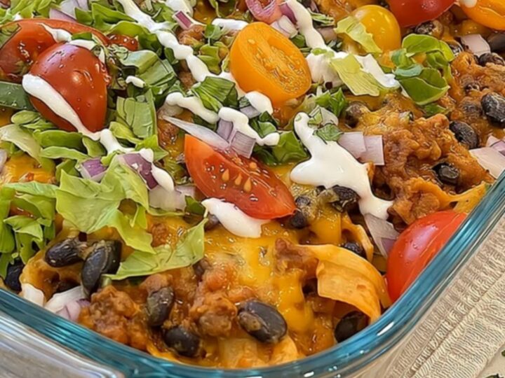 A warm walking taco casserole in a glass dish topped with melted cheese, fresh lettuce, tomatoes, and beans.