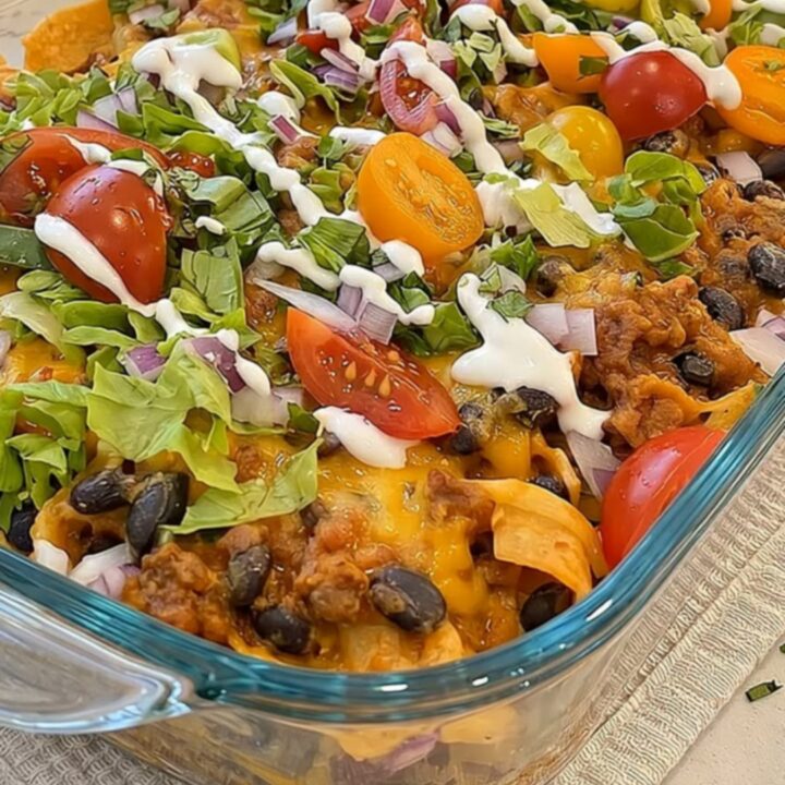 A warm walking taco casserole in a glass dish topped with melted cheese, fresh lettuce, tomatoes, and beans.