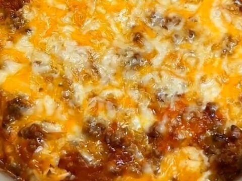 A steaming, cheesy taco hash brown casserole in a grey slow cooker, showing a long, stretchy cheese pull.