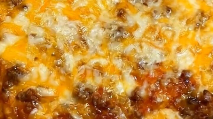 A steaming, cheesy taco hash brown casserole in a grey slow cooker, showing a long, stretchy cheese pull.