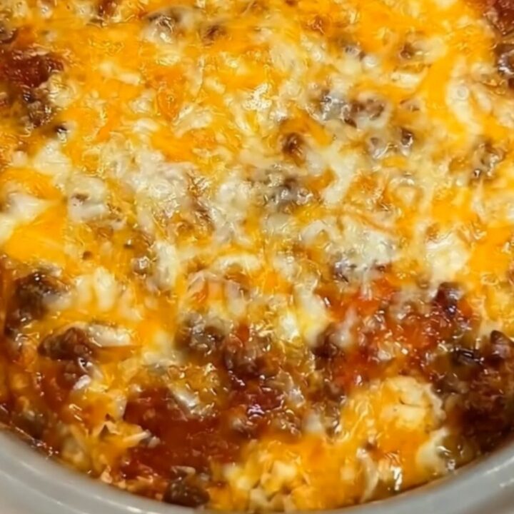 A steaming, cheesy taco hash brown casserole in a grey slow cooker, showing a long, stretchy cheese pull.