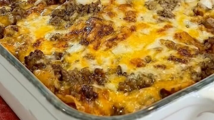 A golden, bubbly beef enchilada casserole in a white dish, showing layers of beef, tortilla, and melted cheese.