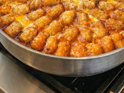 A close-up of a cheesy taco tater tot casserole in a skillet with a portion being lifted by a spatula.