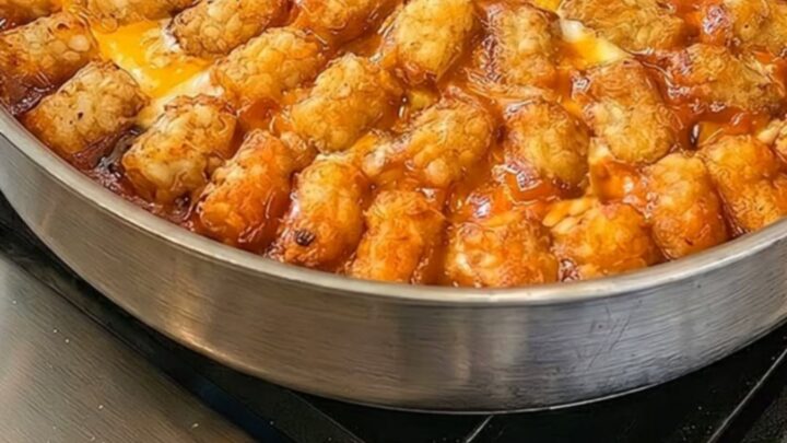 A close-up of a cheesy taco tater tot casserole in a skillet with a portion being lifted by a spatula.