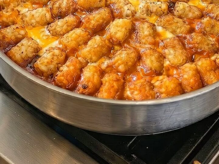 A close-up of a cheesy taco tater tot casserole in a skillet with a portion being lifted by a spatula.