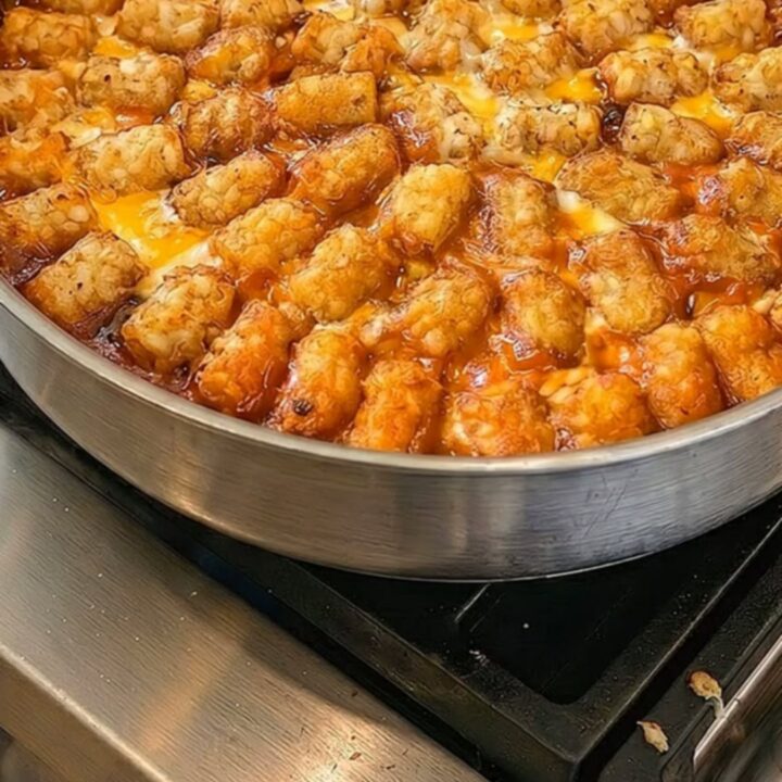 A close-up of a cheesy taco tater tot casserole in a skillet with a portion being lifted by a spatula.