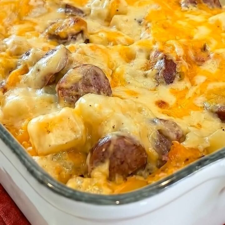 A bubbly, golden-brown cheesy potato and sausage casserole in a white ceramic baking dish.