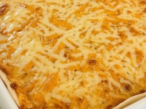 A steaming, golden-brown cheesy taco lasagna served in a white baking dish with a spatula ready to lift a portion.