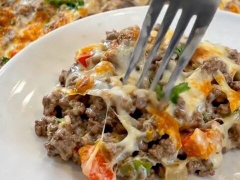 A white casserole dish filled with bubbling ground beef, colorful diced peppers, and golden melted provolone cheese.