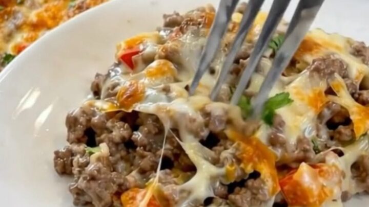 A white casserole dish filled with bubbling ground beef, colorful diced peppers, and golden melted provolone cheese.