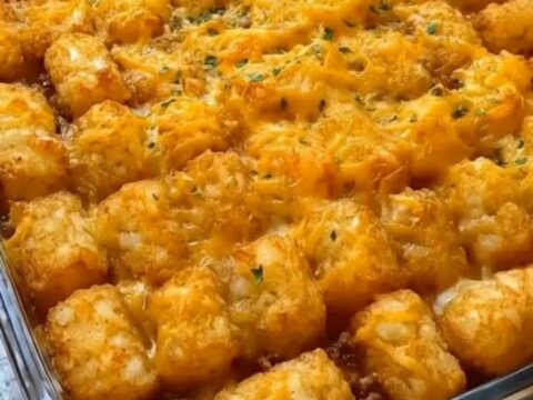 A golden, crispy tater tot casserole in a glass dish with a rich cheese pull.
