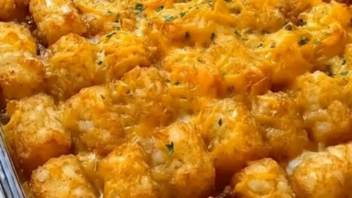 A golden, crispy tater tot casserole in a glass dish with a rich cheese pull.