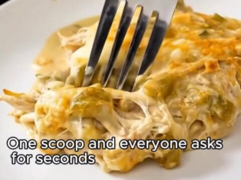 A spatula lifting a portion of creamy green chile chicken enchilada casserole from a glass dish.
